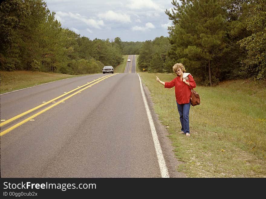 Woman standing beside highway with her thumb out indicating she wants a ride. Woman standing beside highway with her thumb out indicating she wants a ride