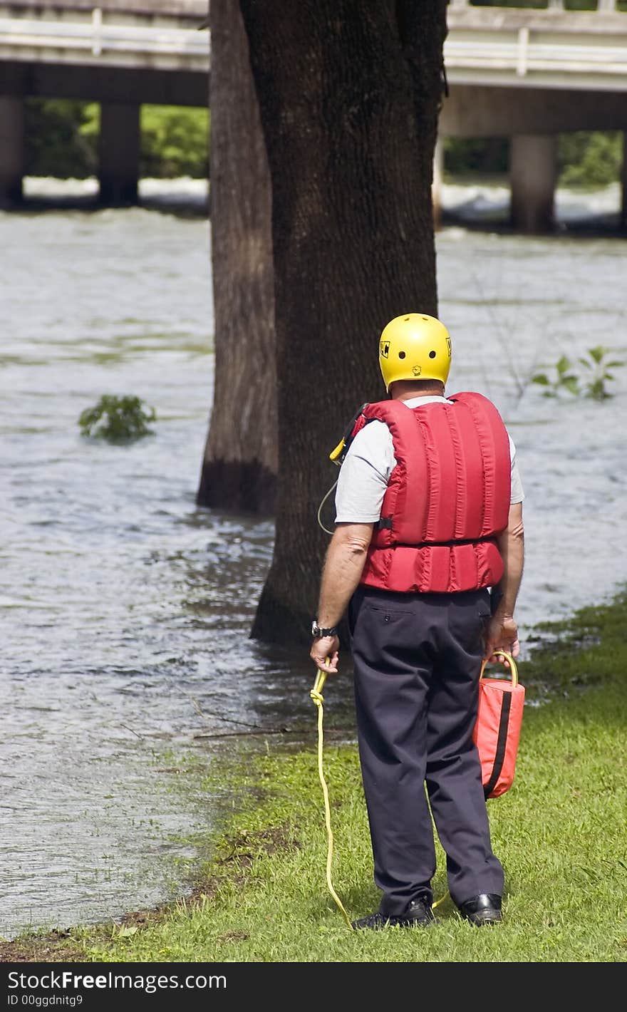 A member of an emergency team standy ready to assist his teammates from the banks of a flooded river. A member of an emergency team standy ready to assist his teammates from the banks of a flooded river.