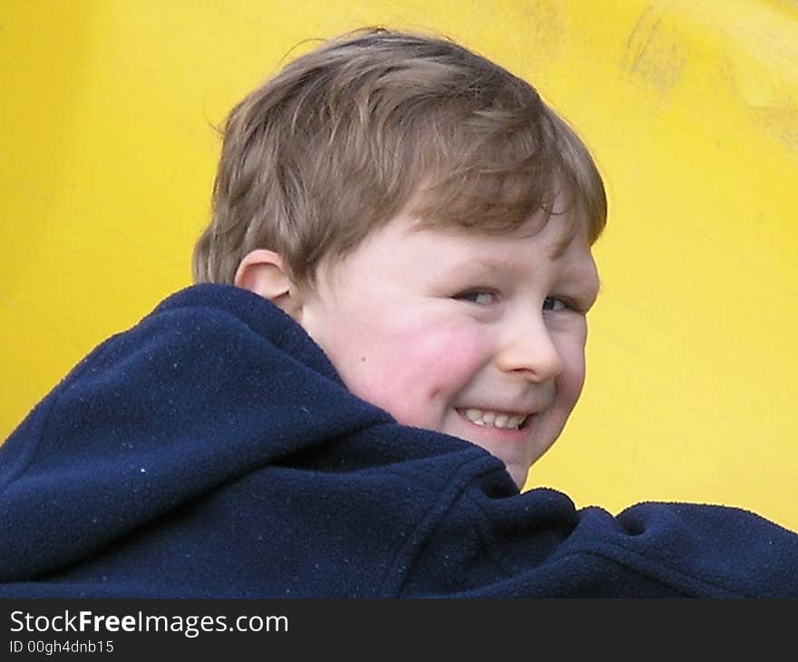 Smiling boy in front of yellow background in blue jacket. Smiling boy in front of yellow background in blue jacket