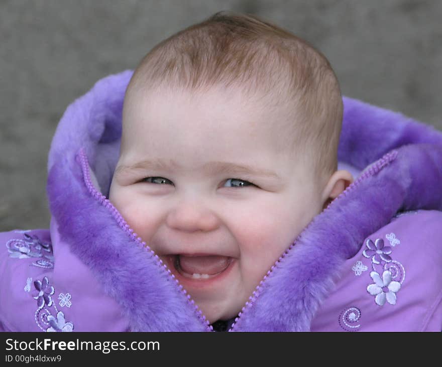 Pretty smiling baby in purple jacket with teeth showing