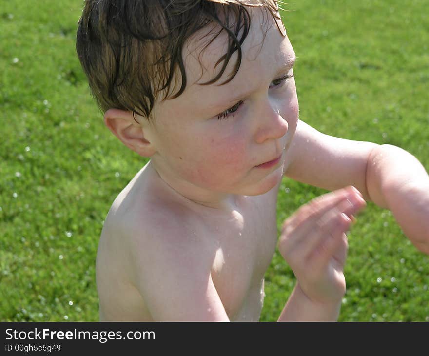 Wet boy playing outside with green grass background. Wet boy playing outside with green grass background