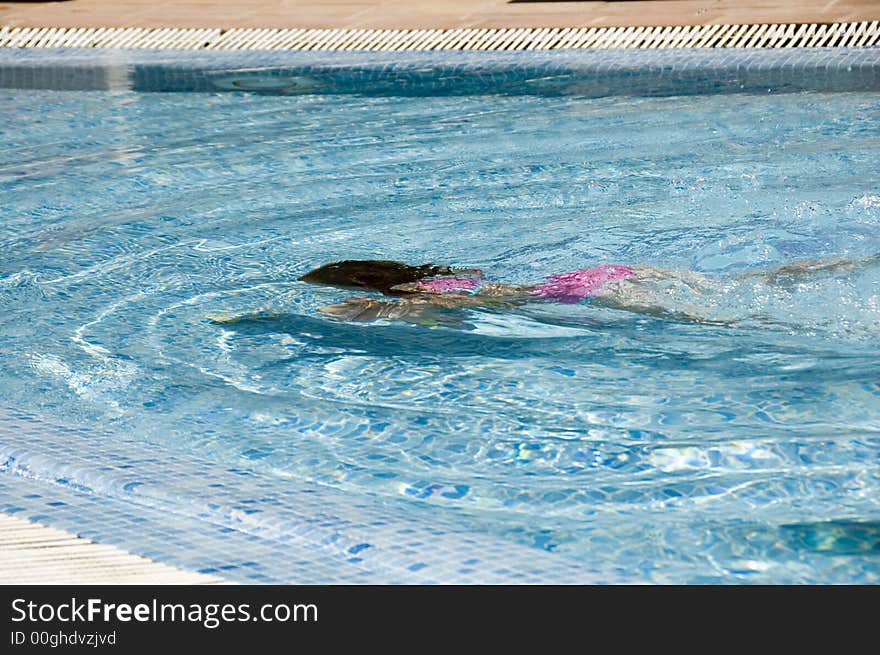 A girl swims underwater in a crystal clear blue pool. A girl swims underwater in a crystal clear blue pool