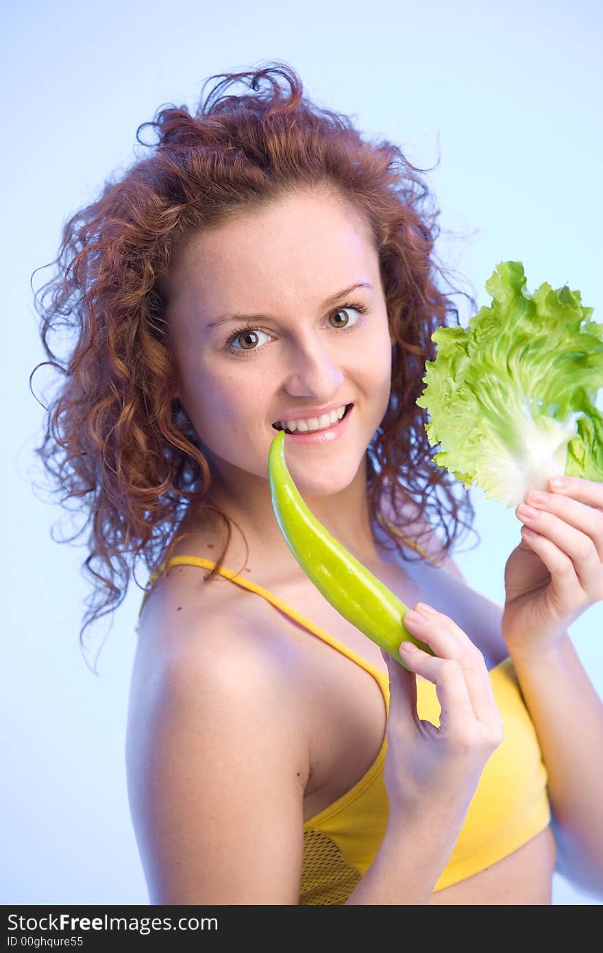 Young happy woman is holding a lettuce leaf and a pepper. Young happy woman is holding a lettuce leaf and a pepper