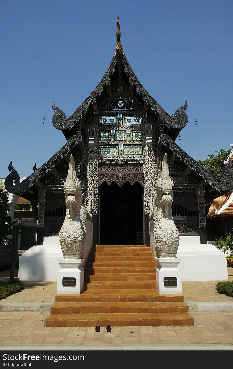 Entry of a buddhist temple in Chiang Mai, north of Thailand. The stairs are covered with tiles. Shoes stay out of the temple. The temple's roof has a lot of ornament, and few lucky bells suspended. On the sides of the stairs are two dragons. Entry of a buddhist temple in Chiang Mai, north of Thailand. The stairs are covered with tiles. Shoes stay out of the temple. The temple's roof has a lot of ornament, and few lucky bells suspended. On the sides of the stairs are two dragons.