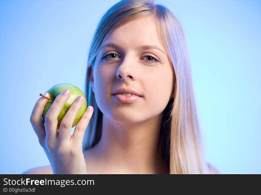 Young blonde woman is holding an apple looking sideways. Young blonde woman is holding an apple looking sideways