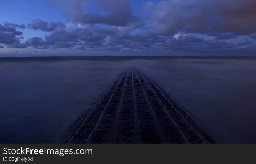 Stone breakwater at Belgian coast at a semi clouded night with a blue-isch atmosphere and milky water due to long exposure