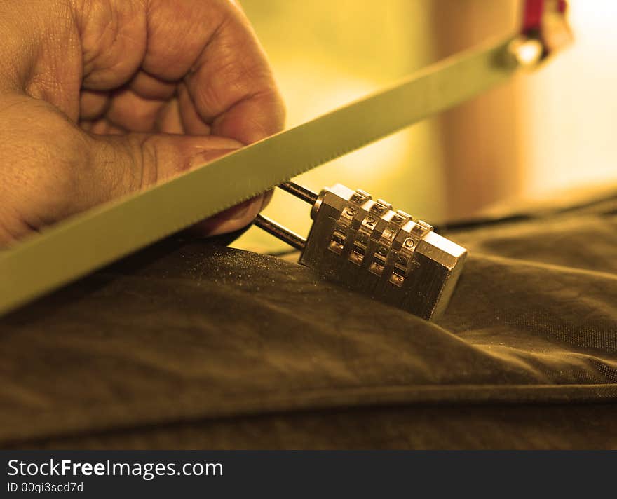 Masculine hand saws a golden padlock in orange color