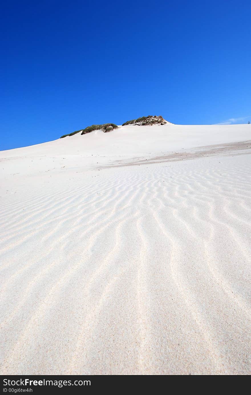 sand dunes on white desert with green hill on the blue sky background. sand dunes on white desert with green hill on the blue sky background