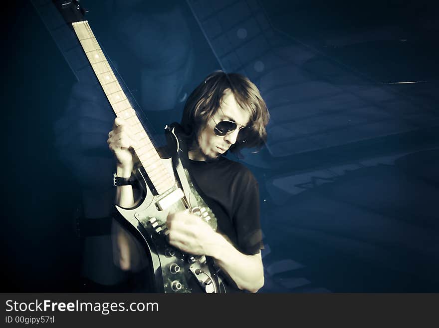 Young man playing electric guitar over blue background, zoom and strobe lighting. Young man playing electric guitar over blue background, zoom and strobe lighting.