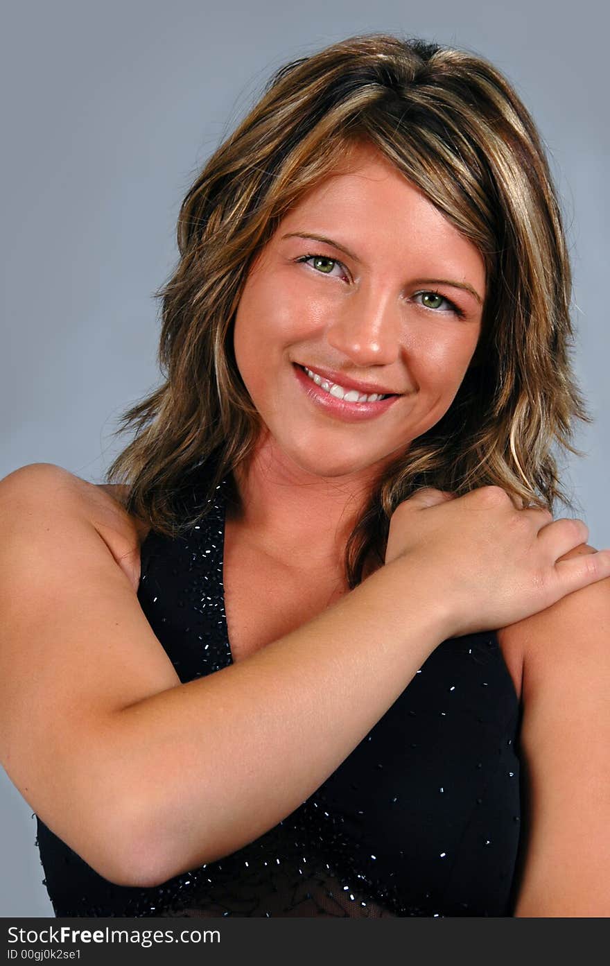 Glamour girl with black gown smiling over a neutral background.