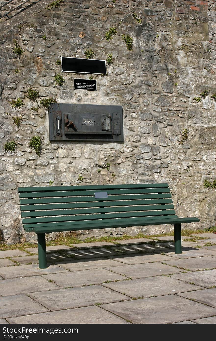 Green bench in a courtyard situated beneath an old cast iron antique bread oven. Green bench in a courtyard situated beneath an old cast iron antique bread oven.