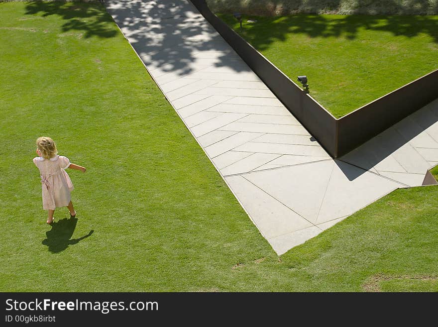 Girl child playing in park with green grass and diagonal sidewalk. Girl child playing in park with green grass and diagonal sidewalk.