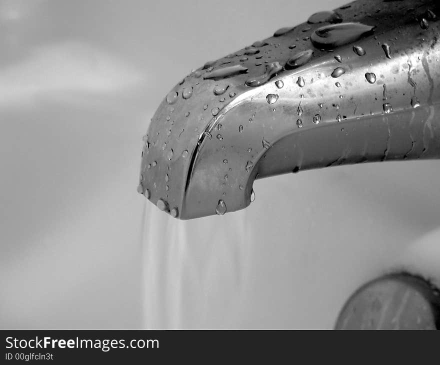 A running bathroom faucet coated in the water droplets of a dripping fixture. A running bathroom faucet coated in the water droplets of a dripping fixture.