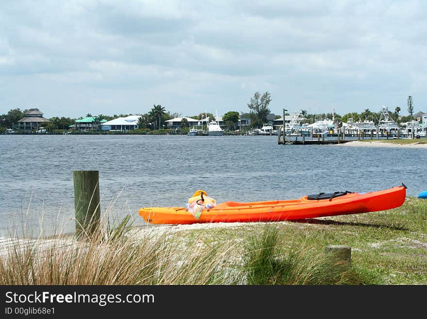 Bright orange and red ocean kayak beached on the riverbank, with contrasting blue sky and blue water.