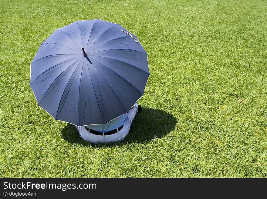 Lonely man sitting in grass with blue umbrella - conceptual