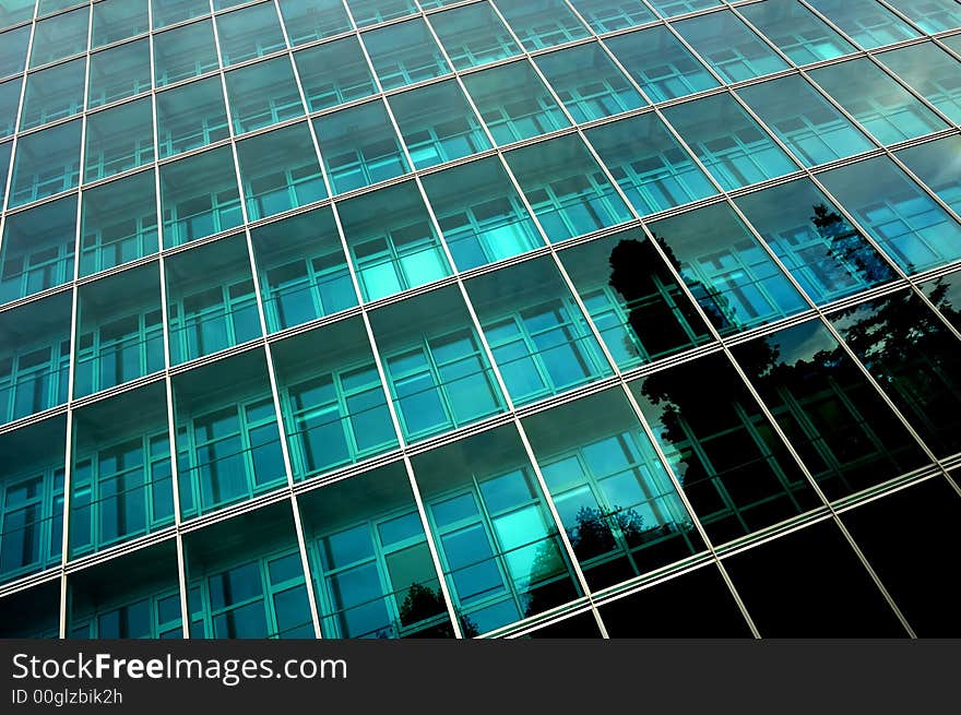 Reflections of trees in the side of a towering, glass-fronted office block