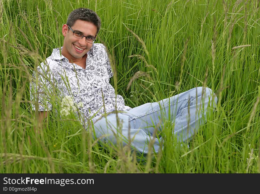 Boy worn eyeglasses sits in high green grass, smiling face. Boy worn eyeglasses sits in high green grass, smiling face