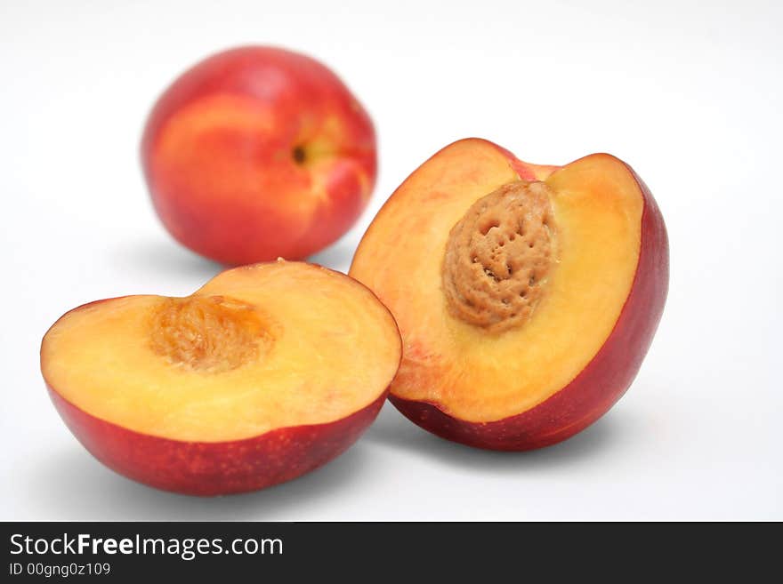 A peach cut in halves with a whole one at the background. A peach cut in halves with a whole one at the background