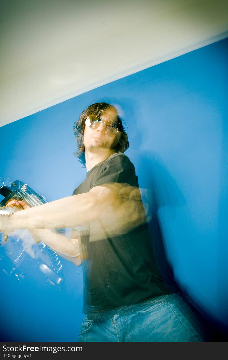 Young man smashing electric guitar over blue background, zoom and strobe lighting. Young man smashing electric guitar over blue background, zoom and strobe lighting.