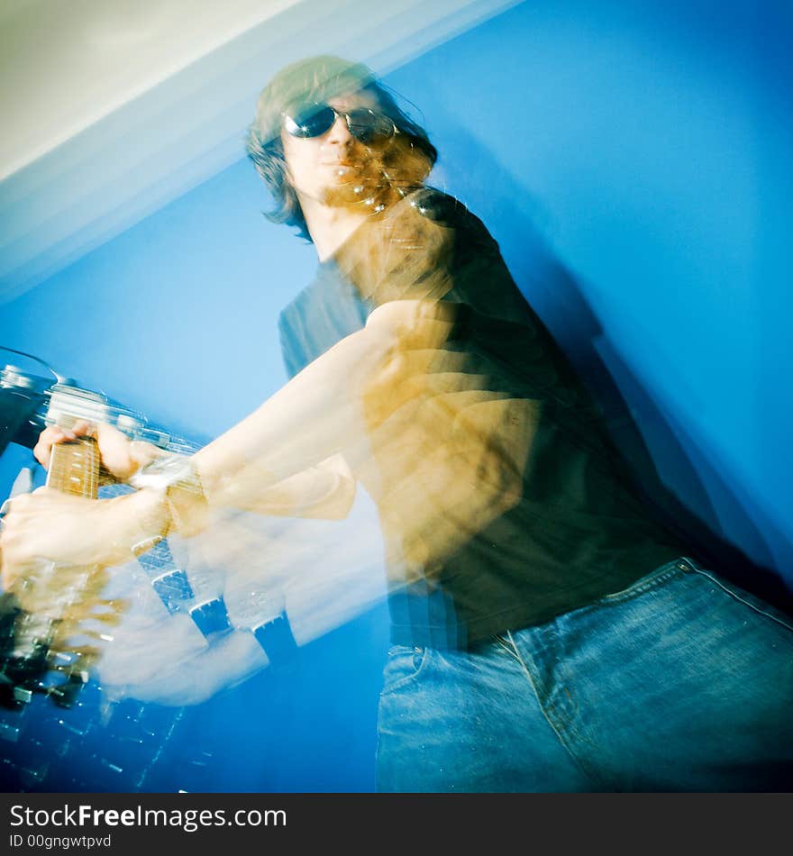 Young man smashing electric guitar over blue background, zoom and strobe lighting. Young man smashing electric guitar over blue background, zoom and strobe lighting.