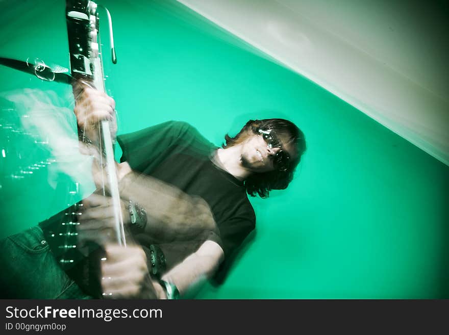 Young man playing electric guitar over green background, zoom and strobe lighting. Young man playing electric guitar over green background, zoom and strobe lighting.