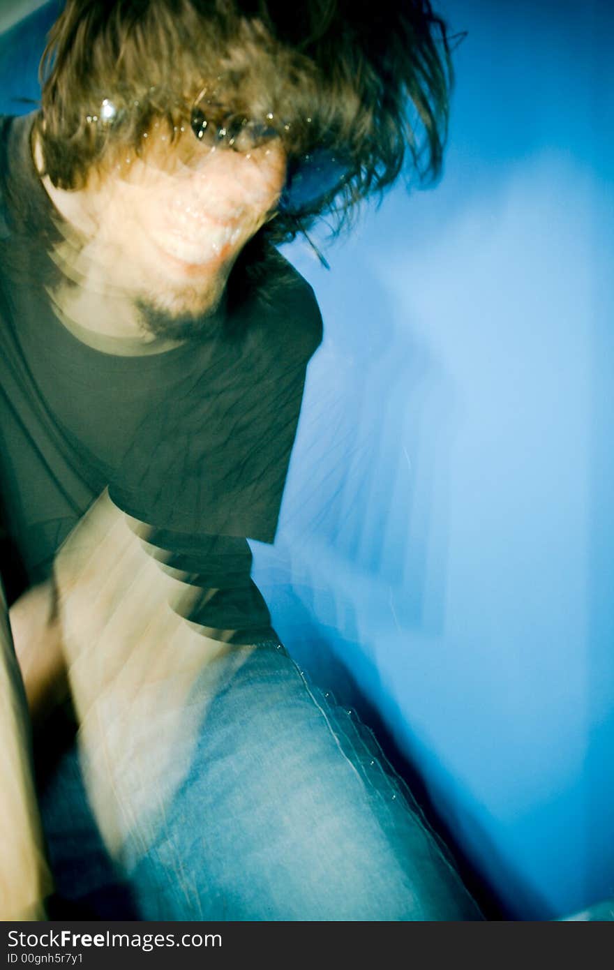 Young man playing electric guitar over blue background, zoom and strobe lighting. Young man playing electric guitar over blue background, zoom and strobe lighting.