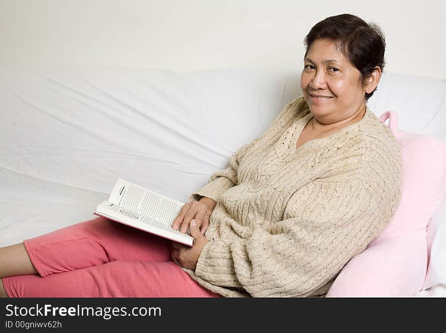 Senior asian woman relaxing at home on the sofa reading a book. Senior asian woman relaxing at home on the sofa reading a book