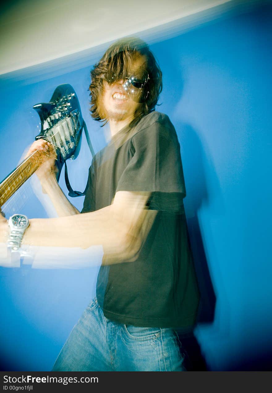 Young man smashing electric guitar over blue background, zoom and strobe lighting. Young man smashing electric guitar over blue background, zoom and strobe lighting.