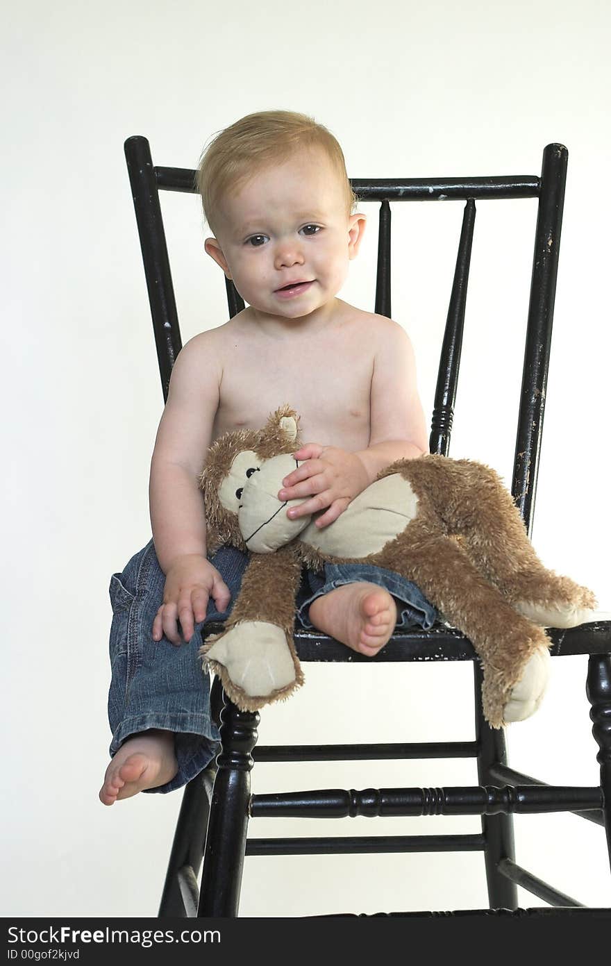 Image of a cute toddler sitting on a black chair, holding a stuffed monkey. Image of a cute toddler sitting on a black chair, holding a stuffed monkey