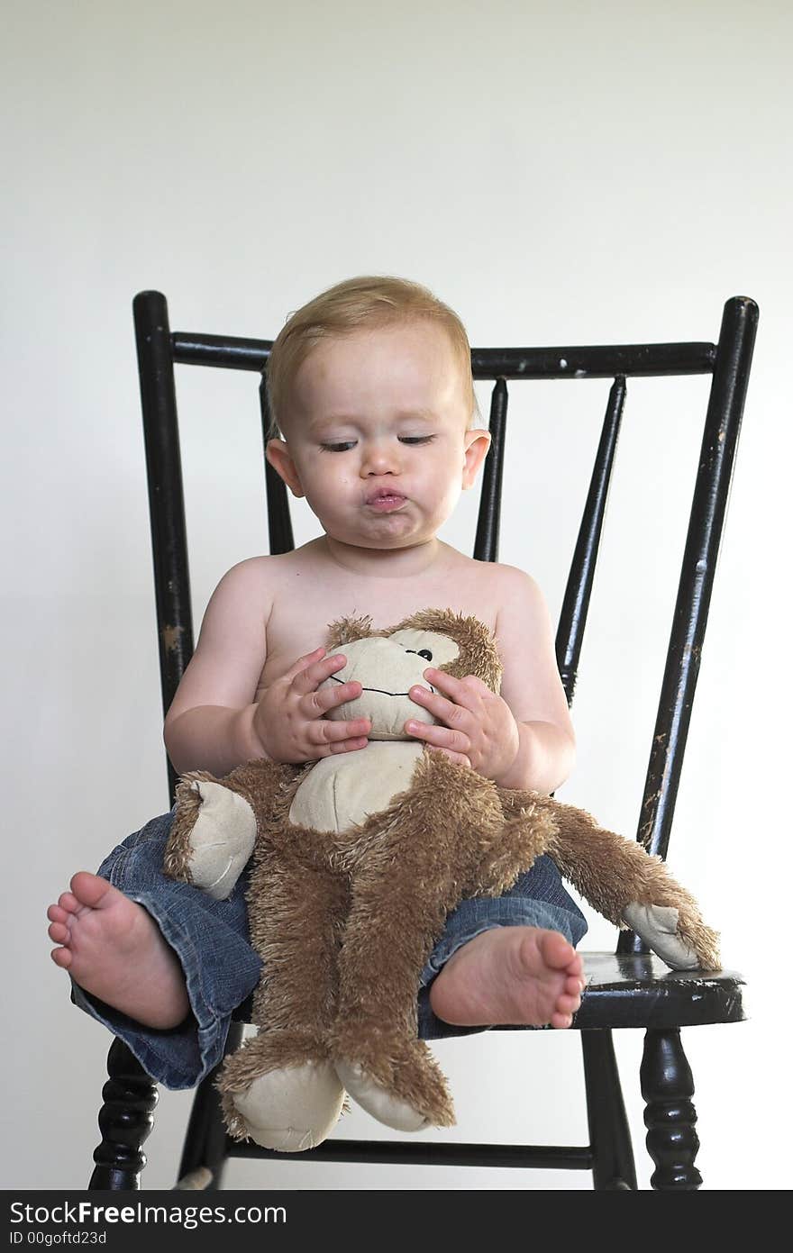 Image of a cute toddler sitting on a black chair, holding a stuffed monkey. Image of a cute toddler sitting on a black chair, holding a stuffed monkey