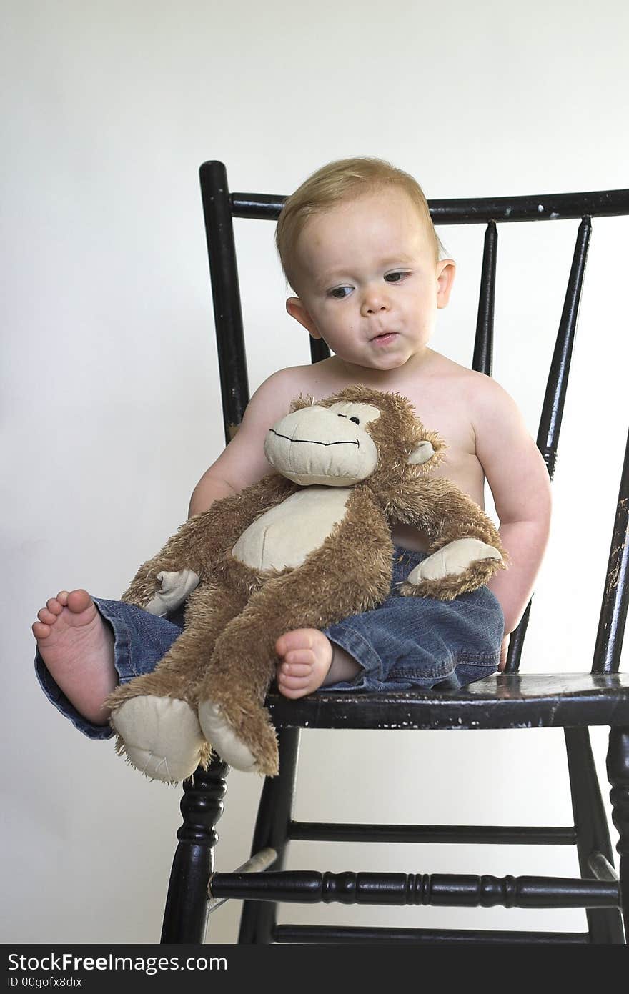 Image of a cute toddler sitting on a black chair, holding a stuffed monkey. Image of a cute toddler sitting on a black chair, holding a stuffed monkey