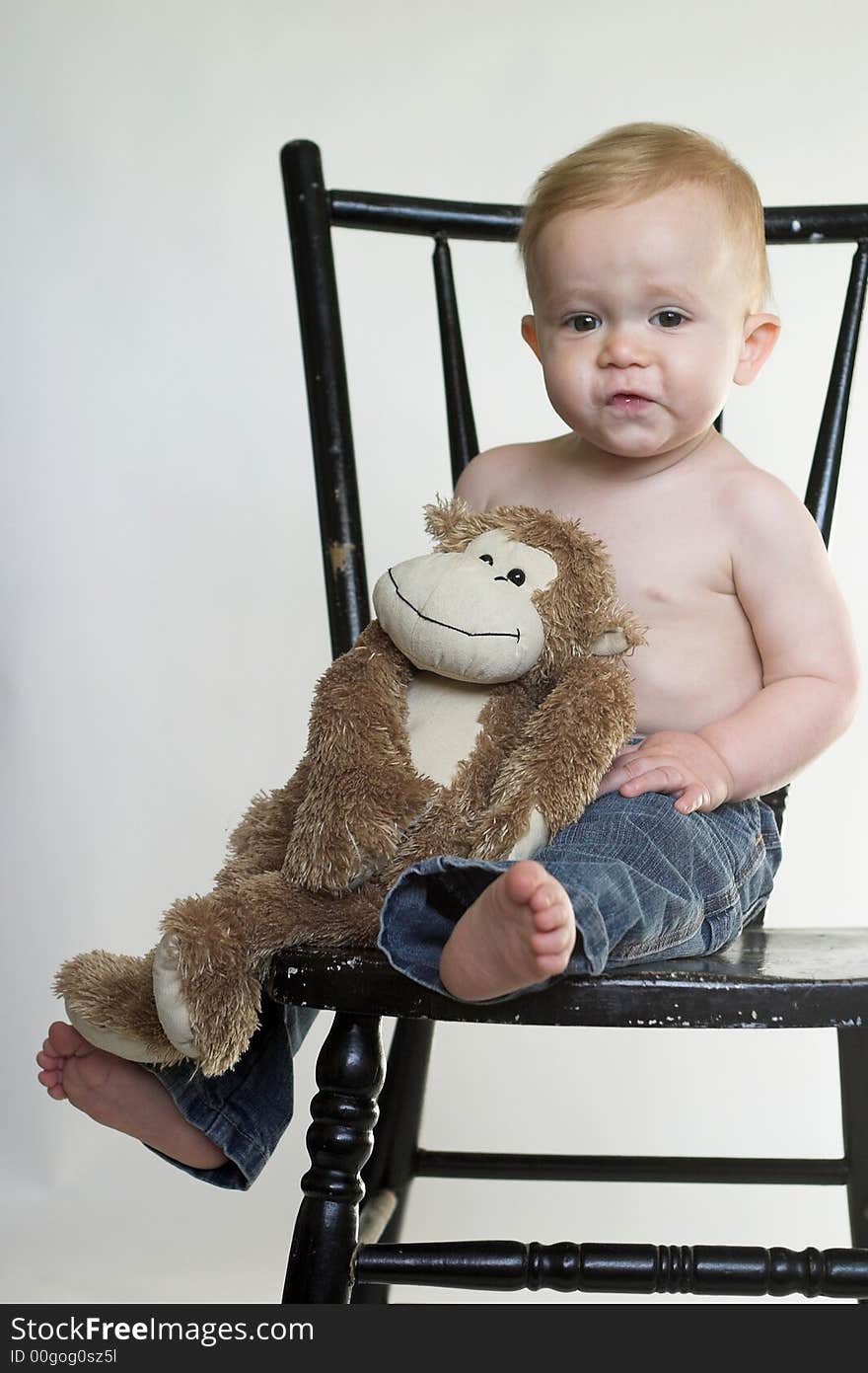 Image of a cute toddler sitting on a black chair, holding a stuffed monkey. Image of a cute toddler sitting on a black chair, holding a stuffed monkey