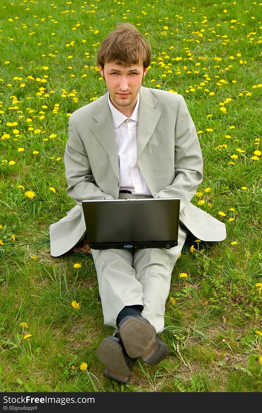 Young caucasian businessman with laptop on green grass background. Young caucasian businessman with laptop on green grass background