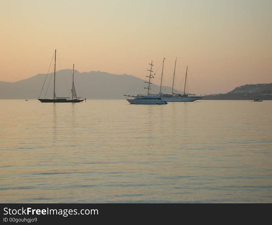 A view of boats/yachts in the Mediterranean island Mykonos during sunset. A view of boats/yachts in the Mediterranean island Mykonos during sunset.