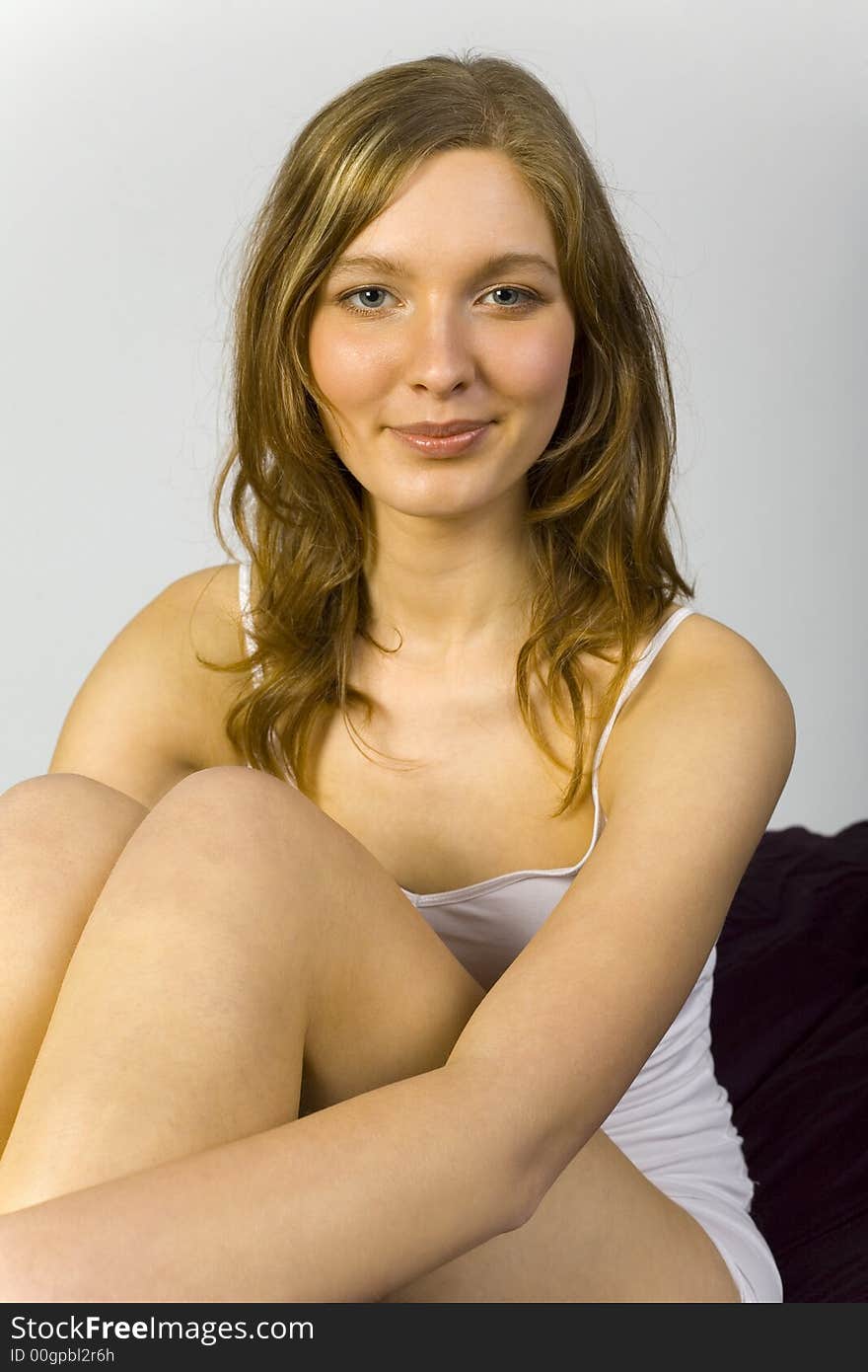 Young, beautiful woman sitting in bed. Smiling, looking at camera. Gray background. Young, beautiful woman sitting in bed. Smiling, looking at camera. Gray background