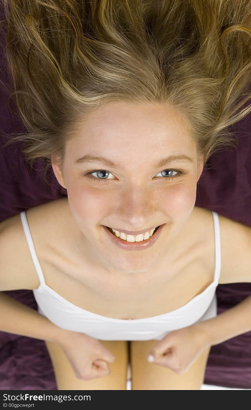 Young, beautiful woman lying in bed on violet coverlet. Smiling, looking at camera. Young, beautiful woman lying in bed on violet coverlet. Smiling, looking at camera