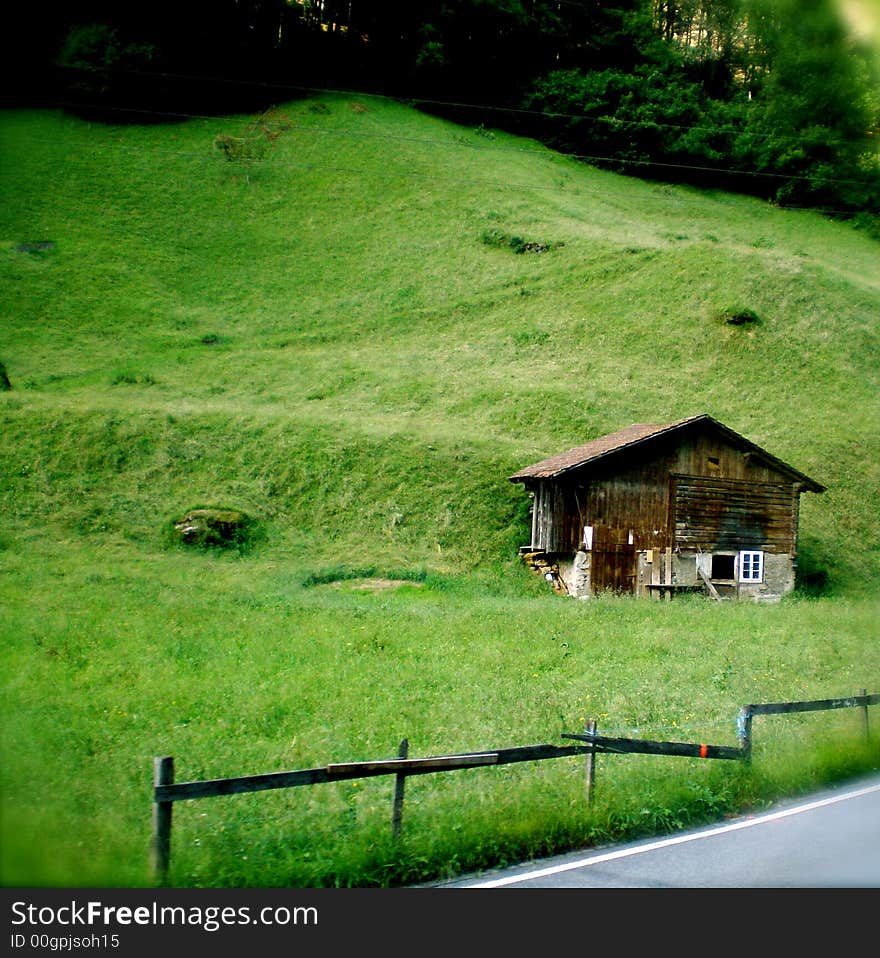 Mountain Cabin in Switzerland on a grassy hill.  Broken fence in front.