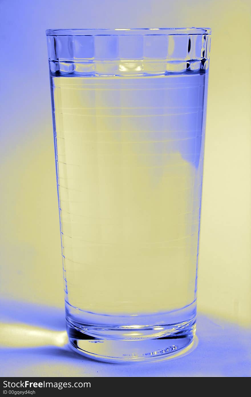 A glass of water with a blue and yellow light on the background. A glass of water with a blue and yellow light on the background.