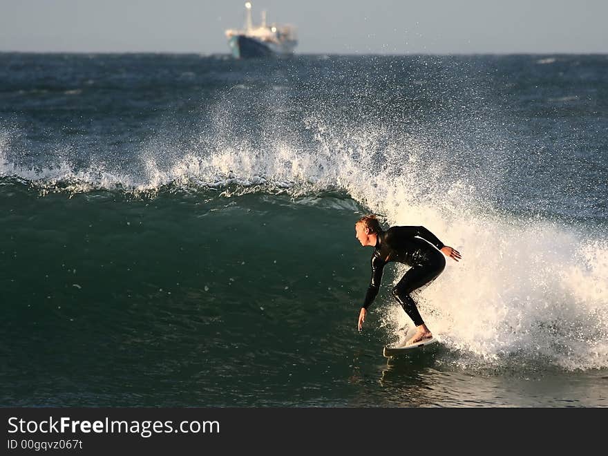 A young lad catching a wave on his surfboard with a ship in the background. A young lad catching a wave on his surfboard with a ship in the background