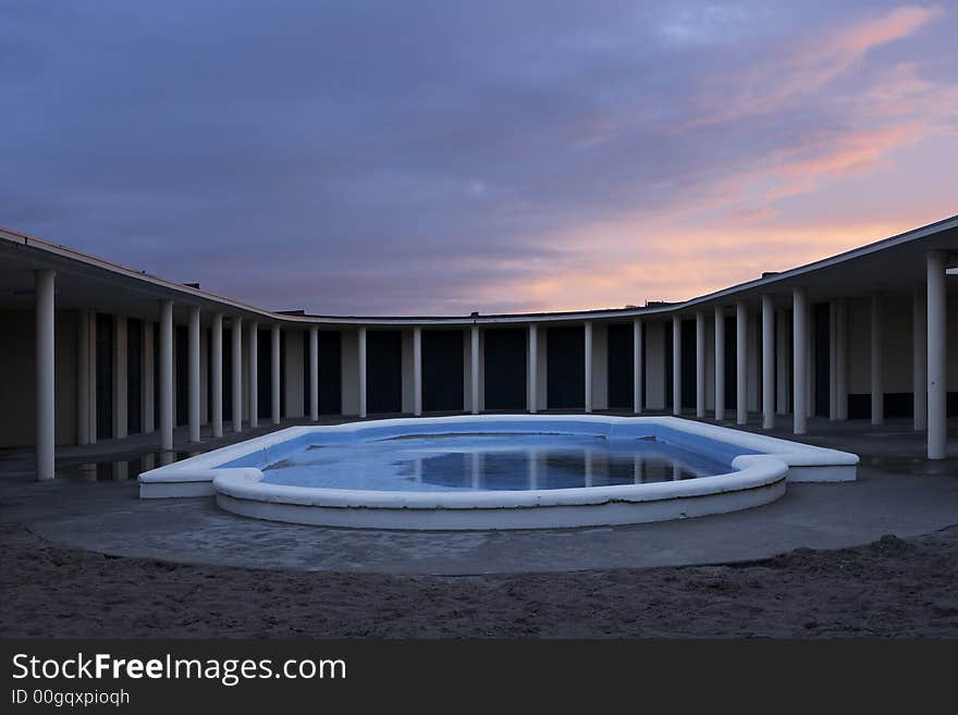 Early morning at Deauville bathouse of the moviestars. The swimming pool in a symmetrical photo with just a bit of water in it and a red sunrise above the colonades. Early morning at Deauville bathouse of the moviestars. The swimming pool in a symmetrical photo with just a bit of water in it and a red sunrise above the colonades.