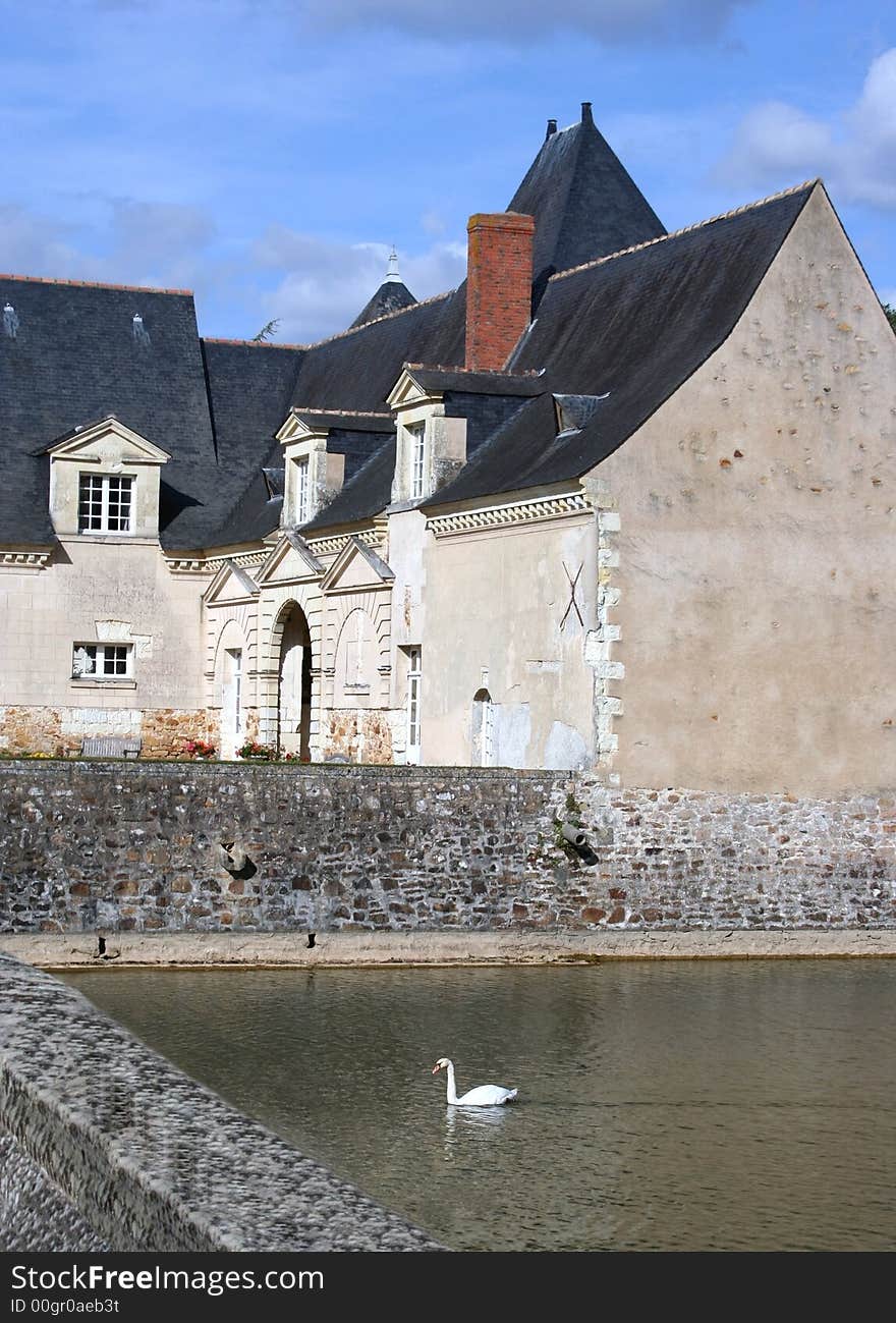 The old stables at Château Plessis-Bourré and a Swan swimming in the moat, France, Europe. The old stables at Château Plessis-Bourré and a Swan swimming in the moat, France, Europe