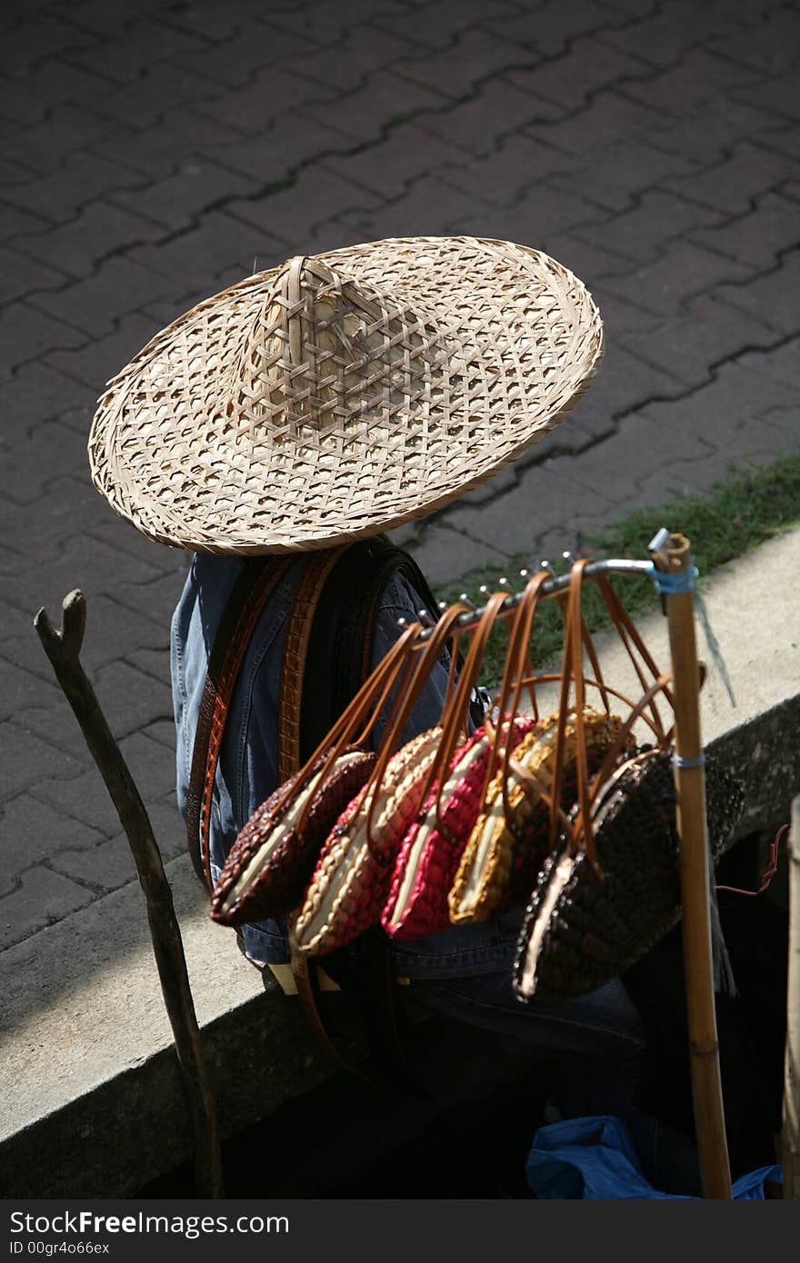 Person selling bags in a Thailand market, wearing a huge hat.