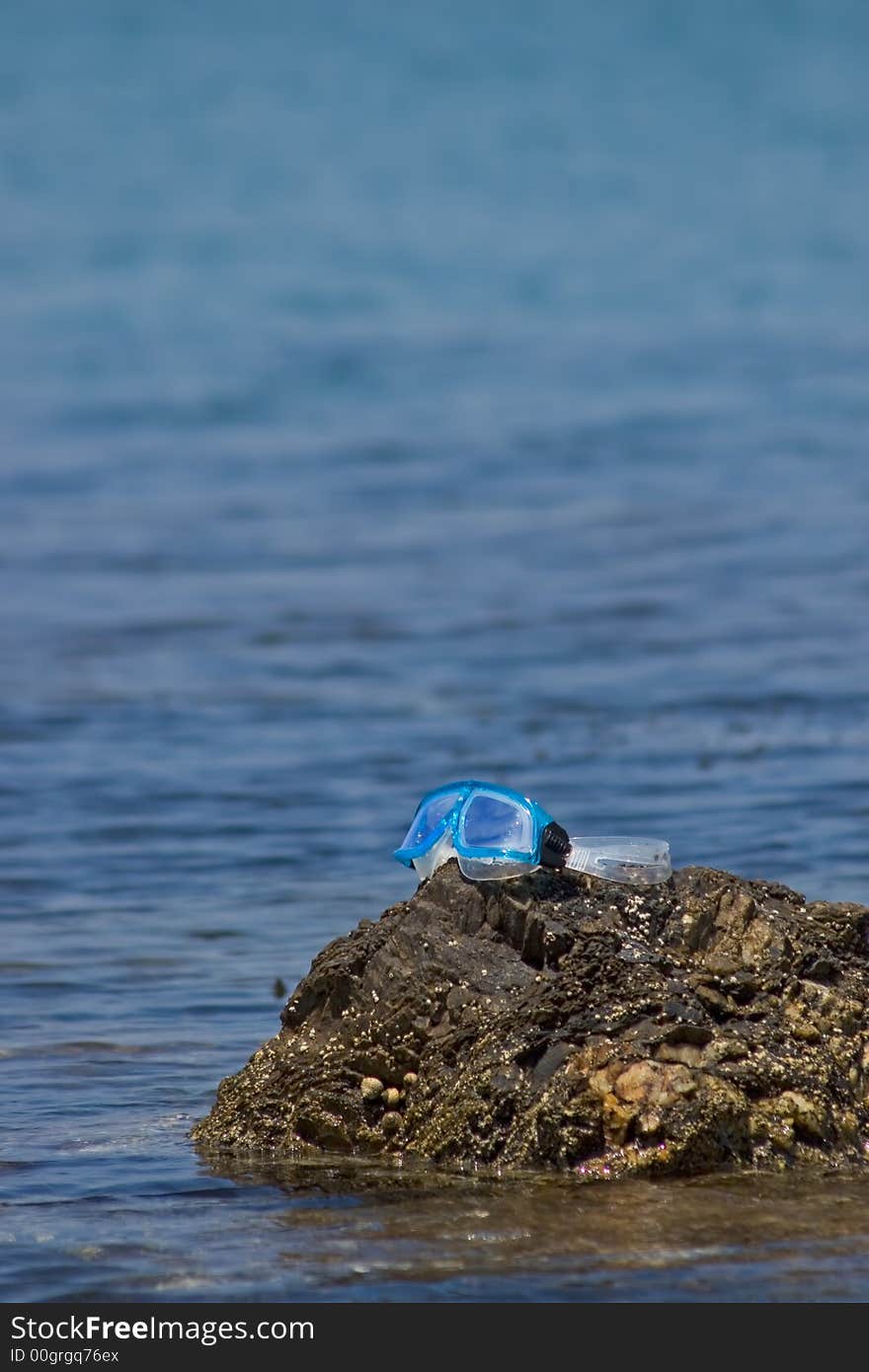 Diving mask posed on a rock at the edge of the sea