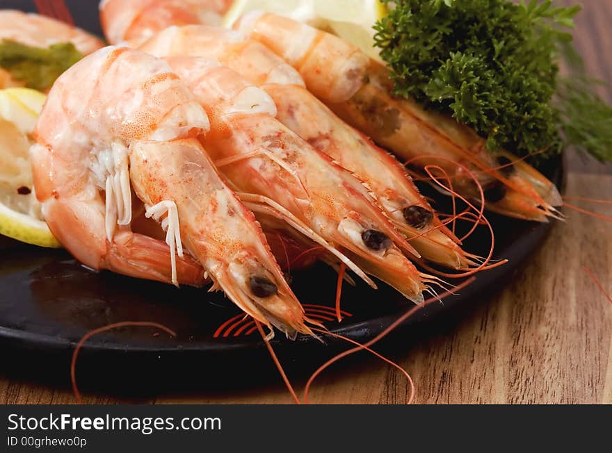 LArge shrimps cooked in shell served on a plate with lemon and greens - closeup