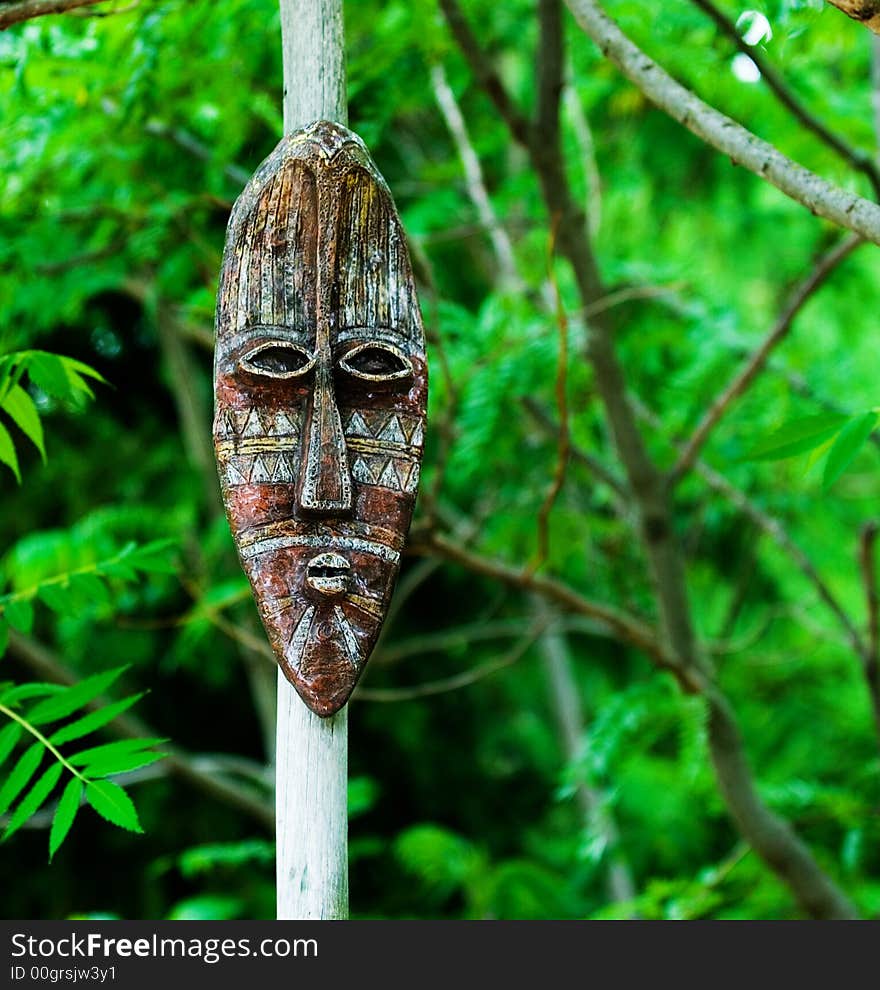 A Tribal mask mounted on a wooden pole with forest background. A Tribal mask mounted on a wooden pole with forest background