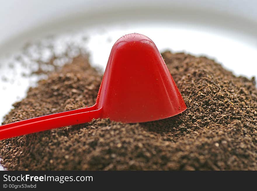 Macro closeup of a red conical coffee scoop with ground coffee poured onto a white plate. Macro closeup of a red conical coffee scoop with ground coffee poured onto a white plate