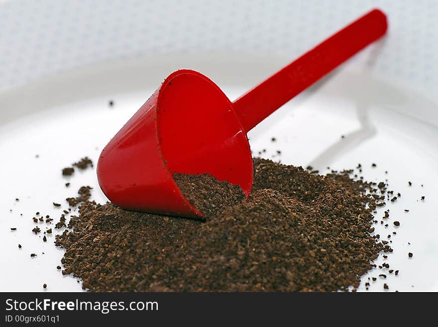 Macro closeup of a red conical coffee scoop with ground coffee poured onto a white plate. Macro closeup of a red conical coffee scoop with ground coffee poured onto a white plate