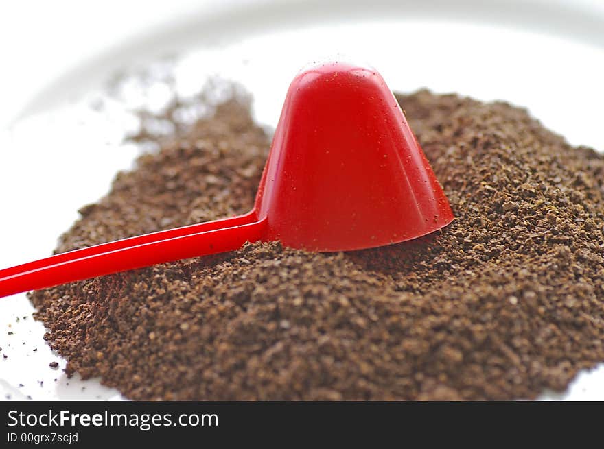 Macro closeup of a red conical coffee scoop with ground coffee poured onto a white plate. Macro closeup of a red conical coffee scoop with ground coffee poured onto a white plate