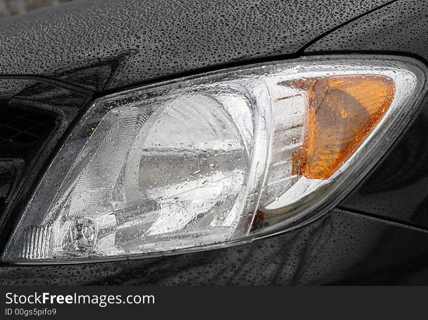 Shiny car with black paint. Water drops on the hood. Car lamp.