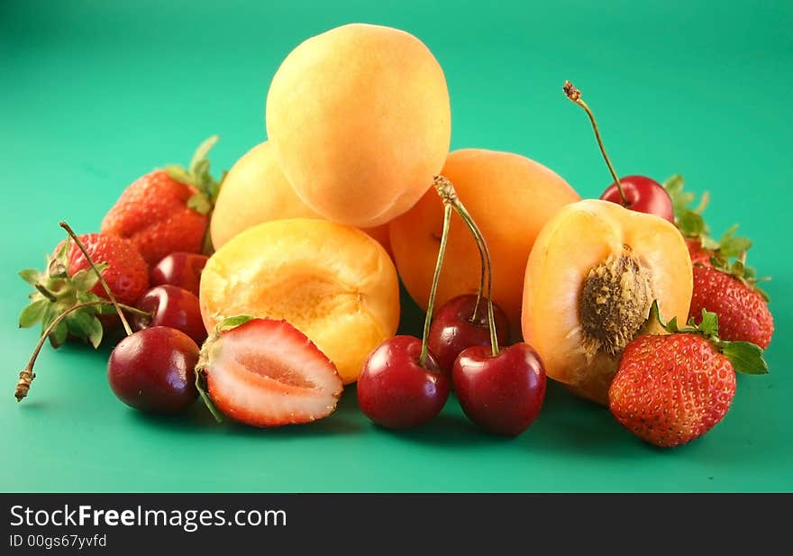 Apricots, sweet cherry  and strawberry is photographed on a green background. Apricots, sweet cherry  and strawberry is photographed on a green background